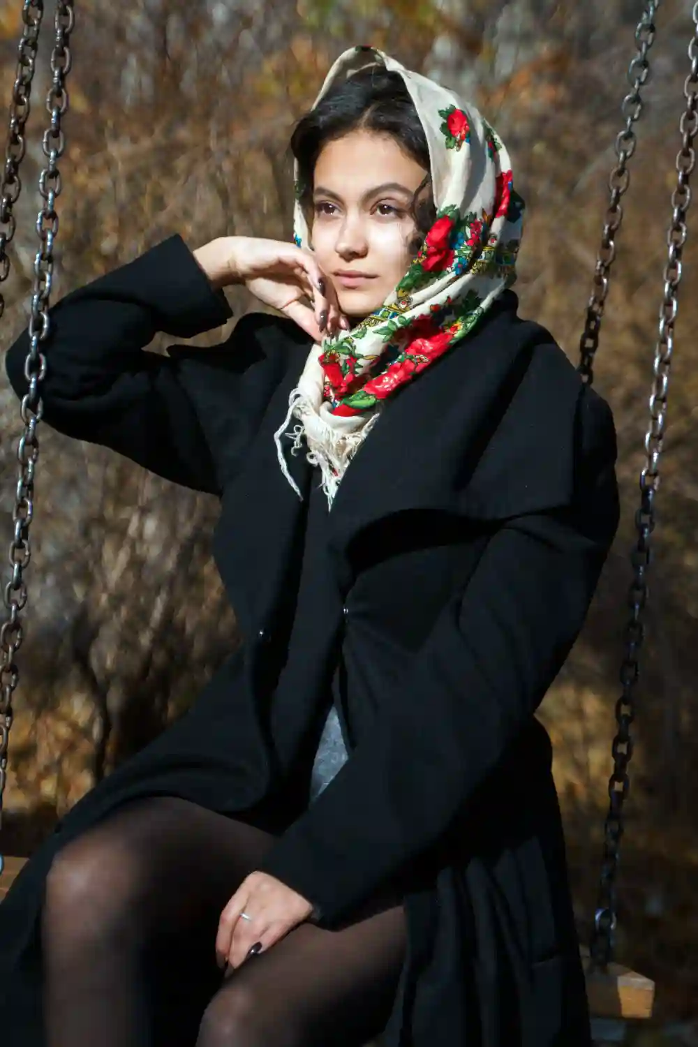 A beautiful girl sits on a swing wearing a traditional Russian headscarf
